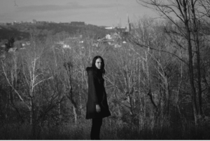 stacy jane grover stands in front of a wooded hillside with a church steeple in the background